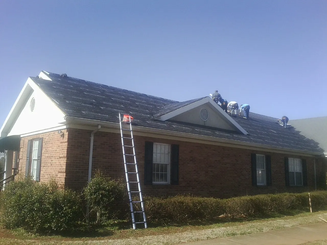 Crew tearing shingles off a brick ranch roof with a ladder set — Metal Roof Repair work by our crew in Bloomfield