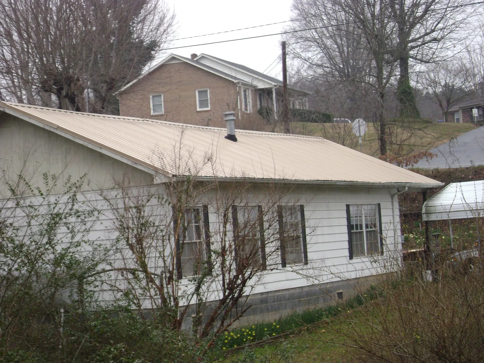 Tan metal roof on a white sided house set into a hillside — Commercial Roofing by Roofing Brothers in Bloomfield